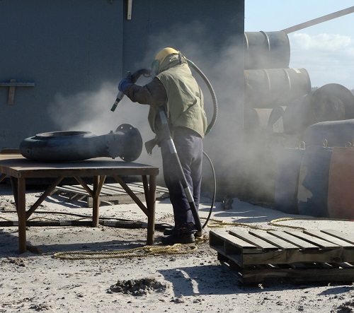 Industrial sandblasting contractor blasting a large steel part outdoors